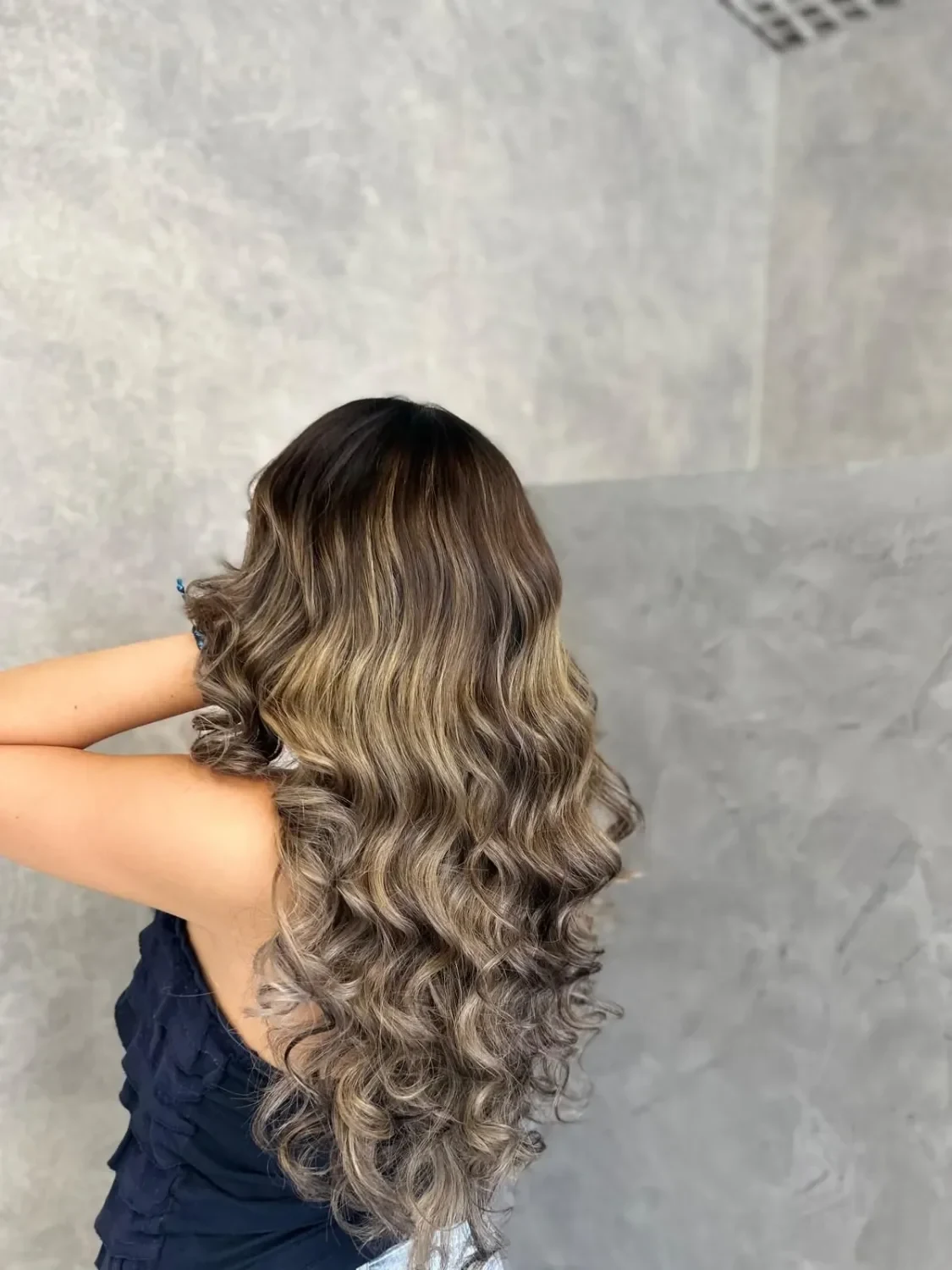 Balayage aus der Antonella Hair Lounge in Ludwigsburg-Mitte: Lange, gewellte Haare von hinten: dunkler Ansatz, der in beigeblonde Längen übergeht