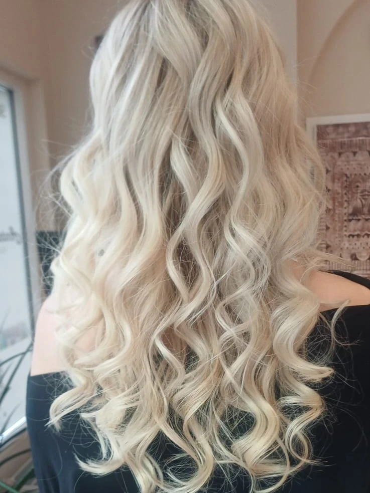 Lange hellblonde Haare mit großen Wellen, von hinten im Salon fotografiert