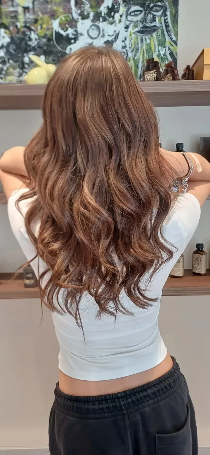 Lange, gewellte Haare in warmem Hellbraun mit karamellfarbenen Spitzen, von hinten fotografiert