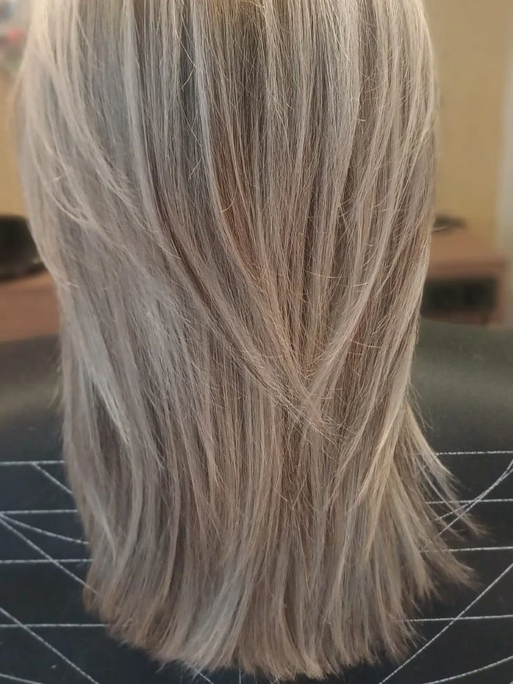 Mittellanges, glattes Haar mit hellblonden Strähnen und Stufenschnitt, von hinten im Salon fotografiert