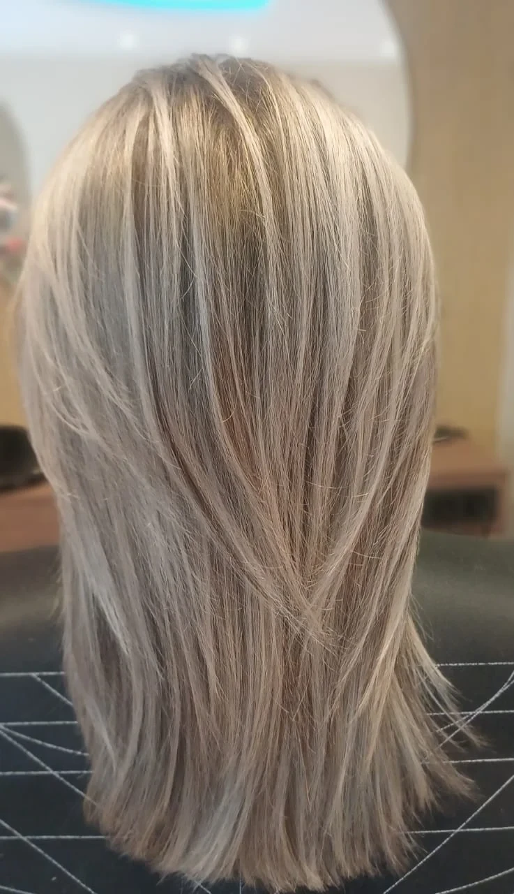 Mittellanges, glattes Haar mit hellblonden Strähnen und Stufenschnitt, von hinten im Salon fotografiert