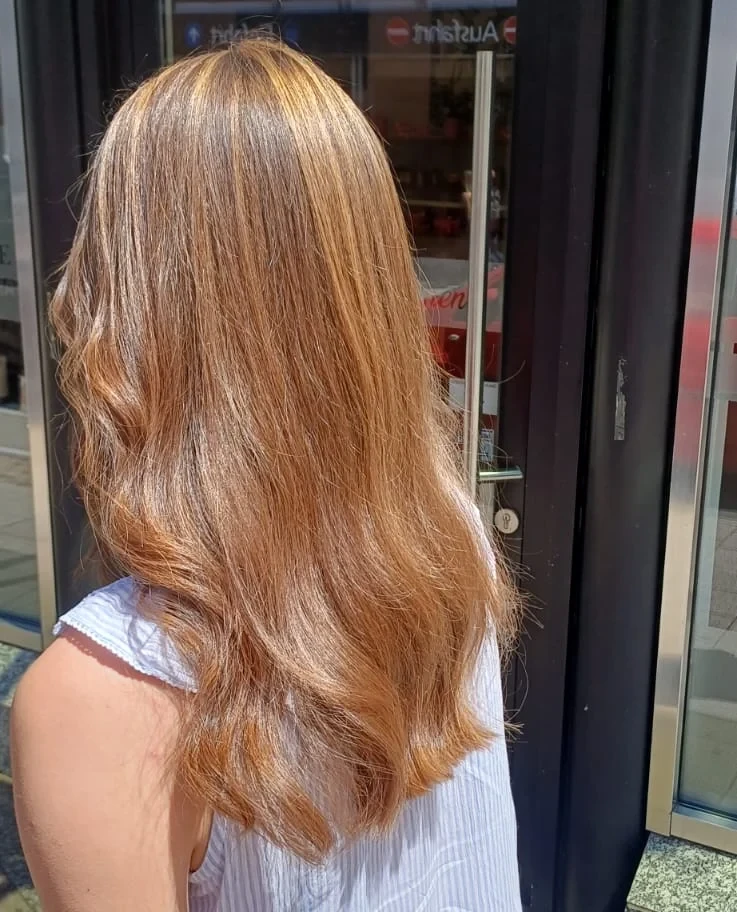 Lange Haare in Karamell- und Kupfertönen mit weichen Wellen, von hinten vor der Salontür fotografiert