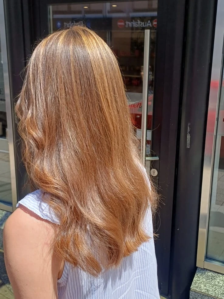 Lange Haare in Karamell- und Kupfertönen mit weichen Wellen, von hinten vor der Salontür fotografiert