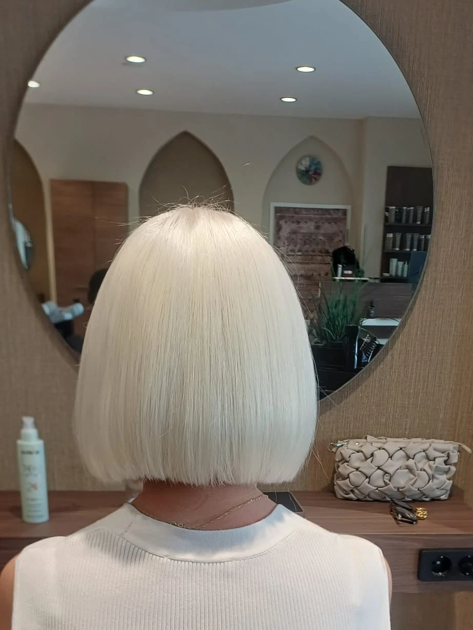 Platinblonder, gerade geschnittener Bob, von hinten vor einem runden Spiegel im Salon fotografiert